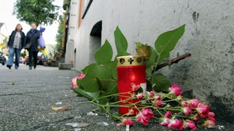 An dem Tatort steht eine Kerze neben Blumen, die auf dem Boden liegen.