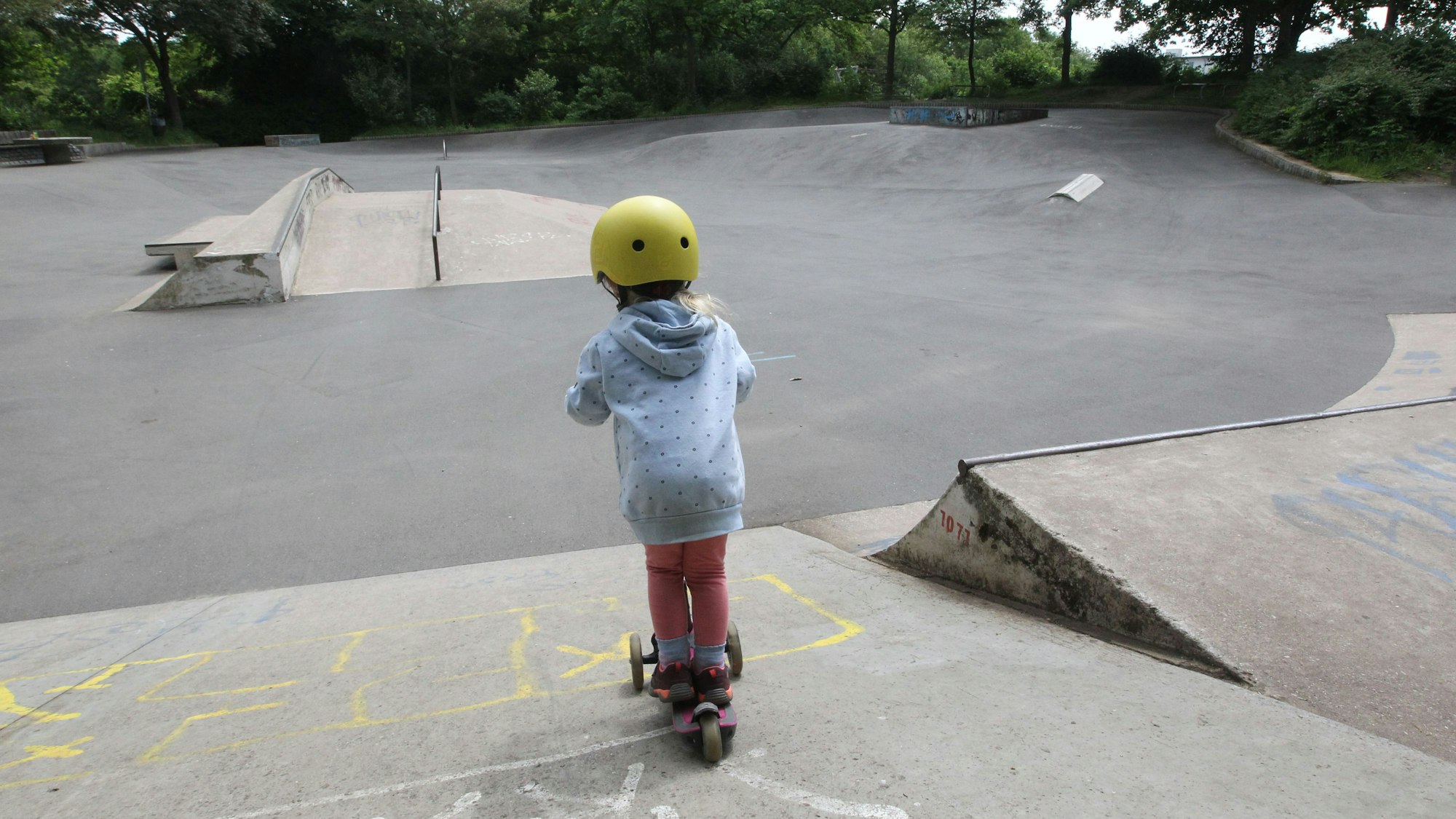 Ein Kind fährt mit einem Roller auf einer Skateanlage.