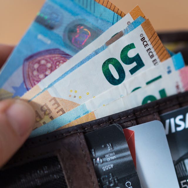 Eine Frau hält eine Geldbörse mit Banknoten und Bankkarten in der Hand.