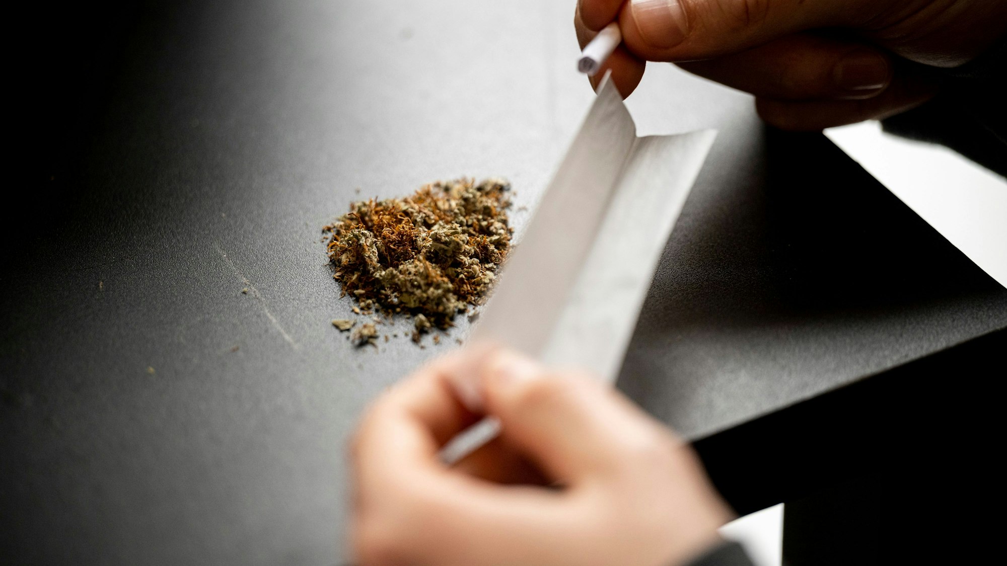 Ein Mann baut einen Joint. Auf der Tischplatte liegt das Marihuana, in den Händen hält der Mann das Papier zum Rollen.