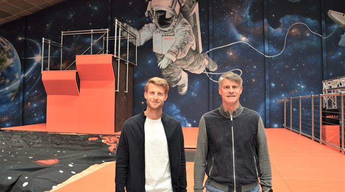 Zwei Männer stehen im Kinderland Aktivi vor einer mit Weltraum-Motiven bemalten Wand.&nbsp;