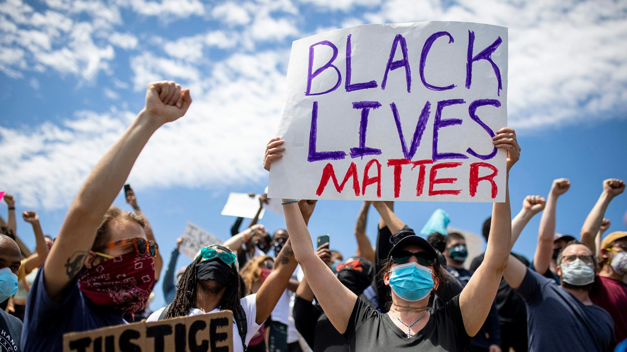 Demonstrierende sind auf der Straße nach dem Tod von George Floyd unterwegs. Eine Frau hält ein „Black Lives Matter“-Schild in die Luft.