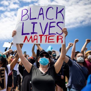 Demonstrierende sind auf der Straße nach dem Tod von George Floyd unterwegs. Eine Frau hält ein „Black Lives Matter“-Schild in die Luft.