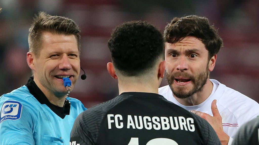 FC-Kapitän Jonas Hector während einer Auseinandersetzung mit Augsburgs Ruben Vargas und Schiedsrichter Patrick Ittrich.