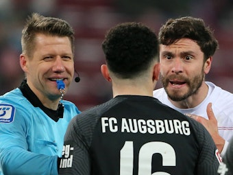 FC-Kapitän Jonas Hector während einer Auseinandersetzung mit Augsburgs Ruben Vargas und Schiedsrichter Patrick Ittrich.