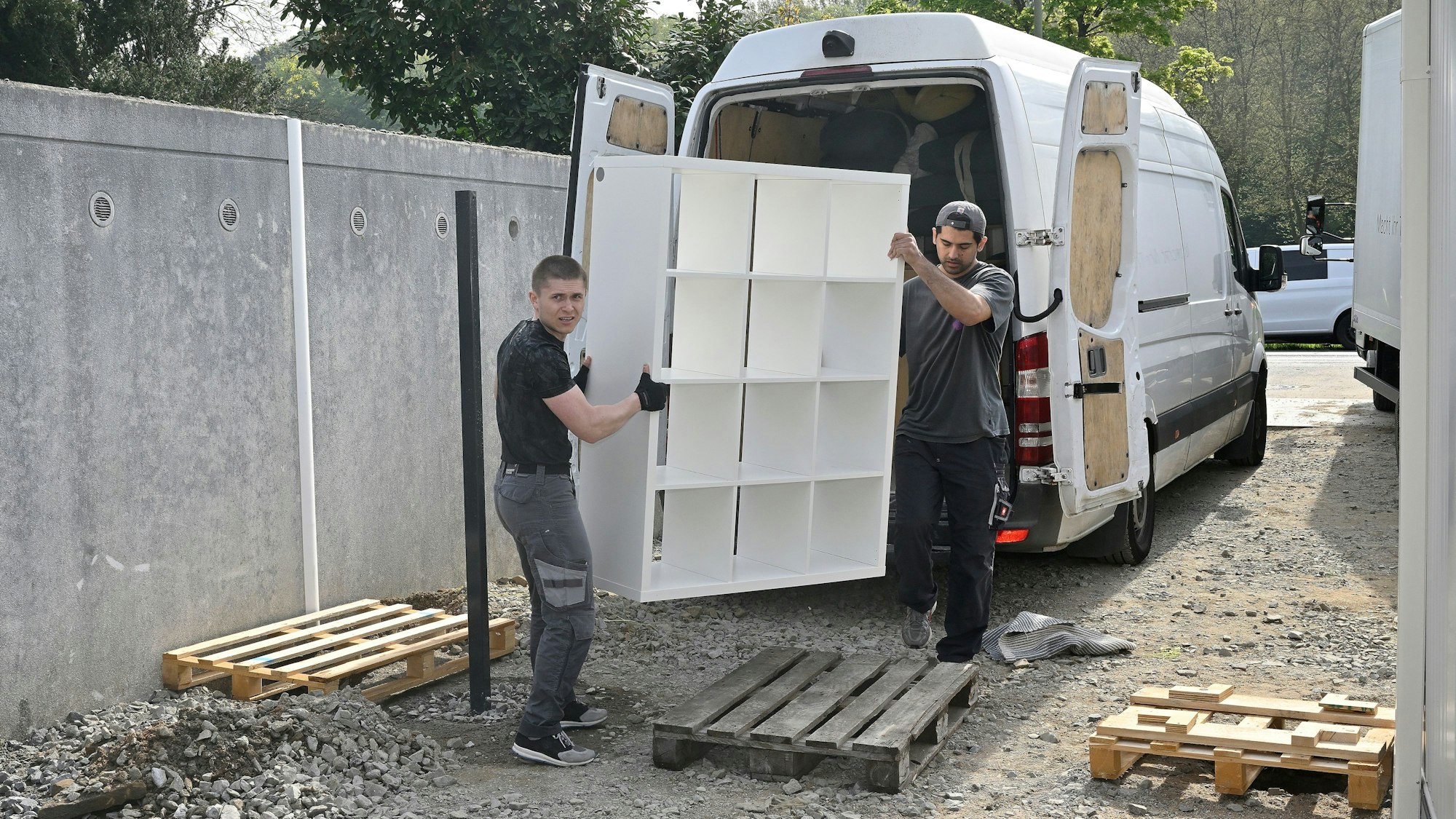 Der Umzug der Kita Kobolde in die neue Containeranlage. Zwei Männer laden ein Regal aus einem Lieferwagen aus.