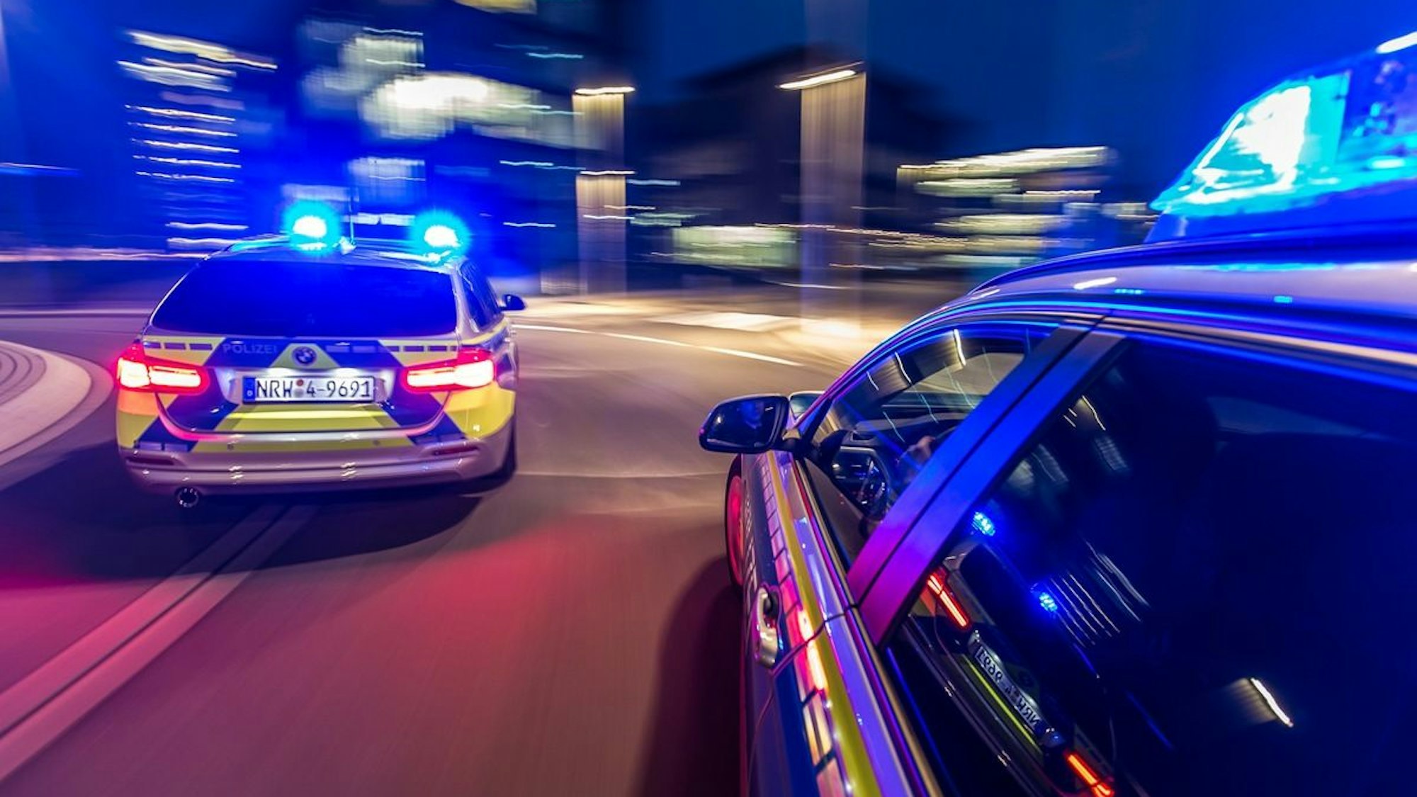 Zwei Polizeiwagen rasen mit Blaulicht durch die Nacht.