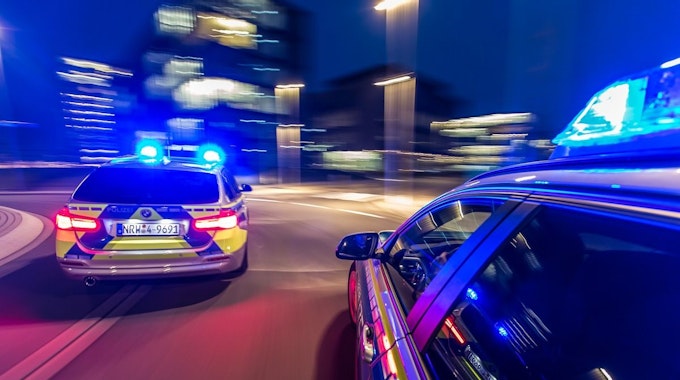 Zwei Polizeiwagen rasen mit Blaulicht durch die Nacht.