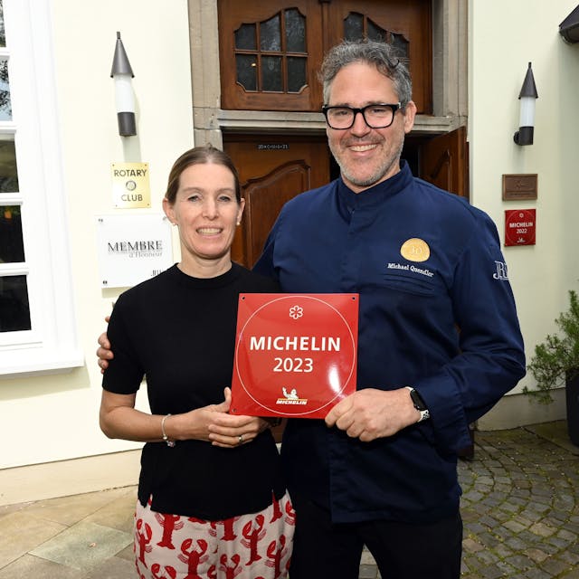Ein Koch und seine Frau stehen nebeneinander und halten die Auszeichnung „Michelin 2023“ in den Händen.