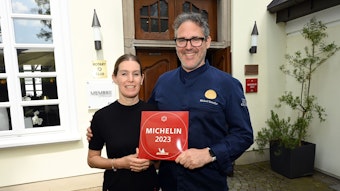 Ein Koch und seine Frau stehen nebeneinander und halten die Auszeichnung „Michelin 2023“ in den Händen.