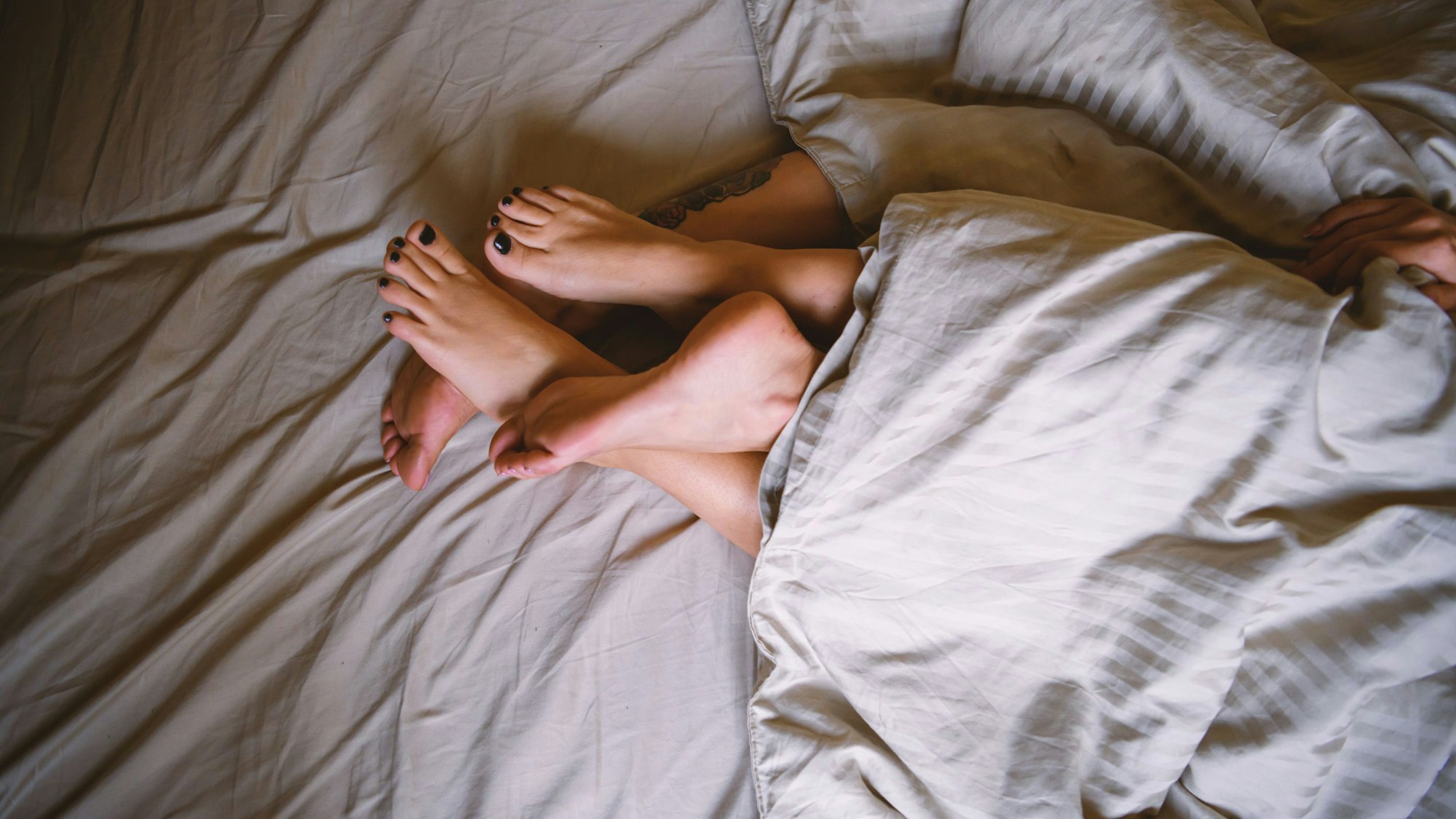 Zwei Paar Füße ragen am Ende einer Bettdecke hervor