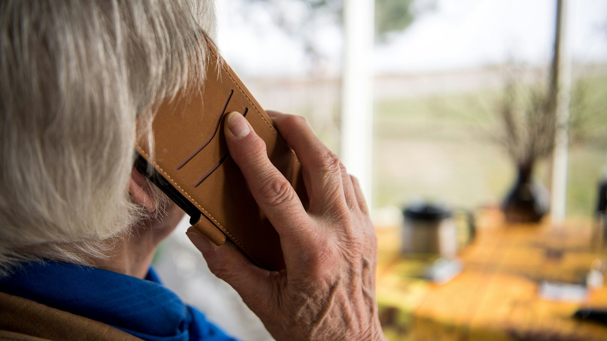 Eine ältere Frau ist von hinten mit einem Telefonhörer am Ohr zu sehen.