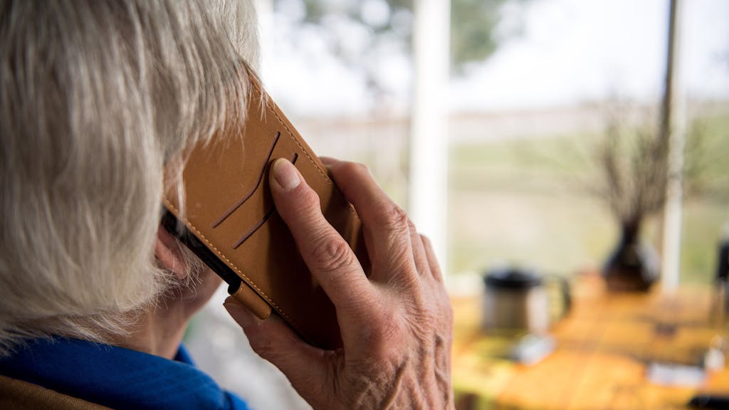Eine ältere Frau ist von hinten mit einem Telefonhörer am Ohr zu sehen.
