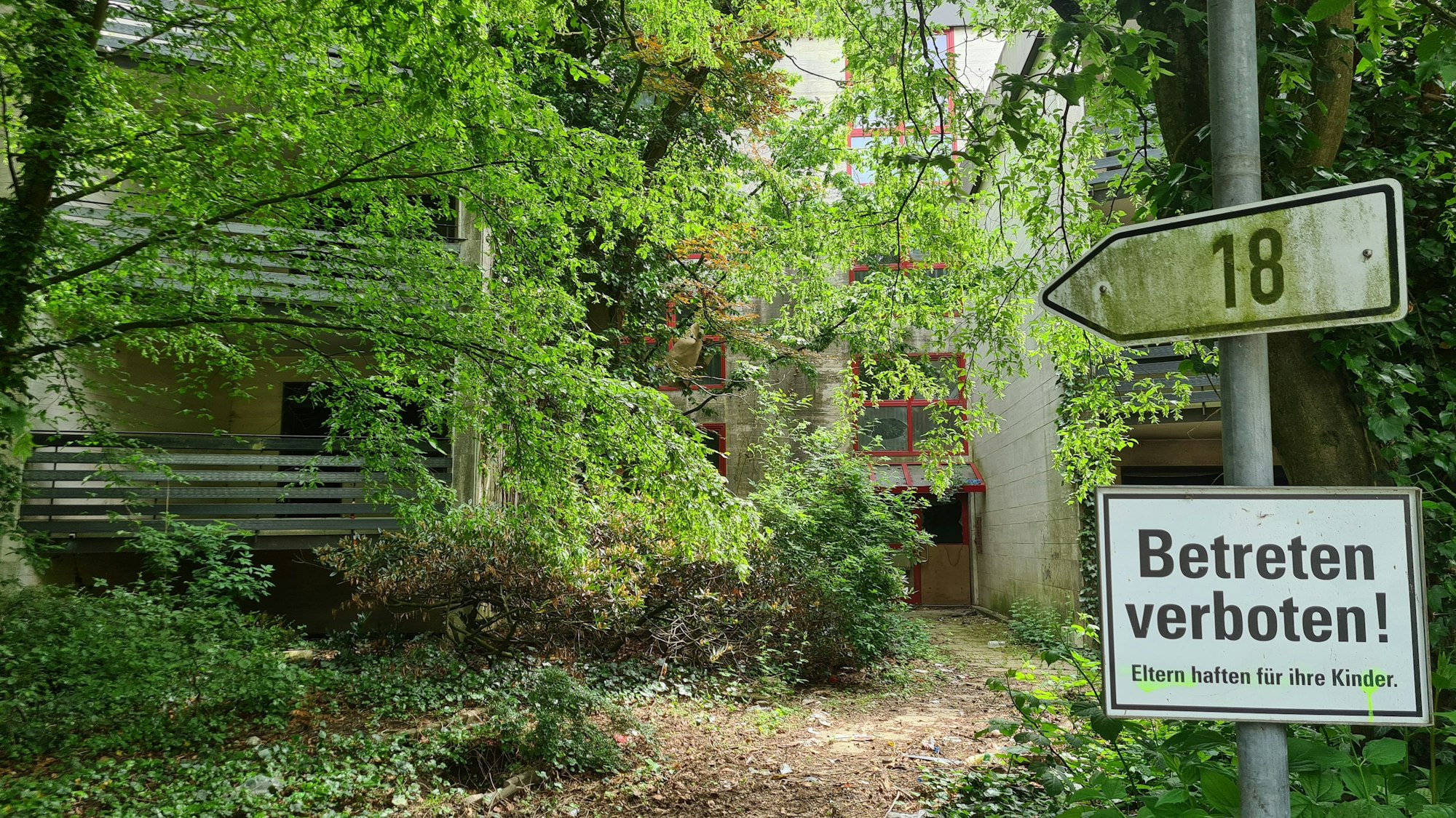 Auf dem Foto sind Balkone und der Eingang des Hauses mit der Nummer 18 zu sehen. Ein Schild weist den Weg dorthin. Auf einem anderen ist „Betreten verboten!“ zu lesen.