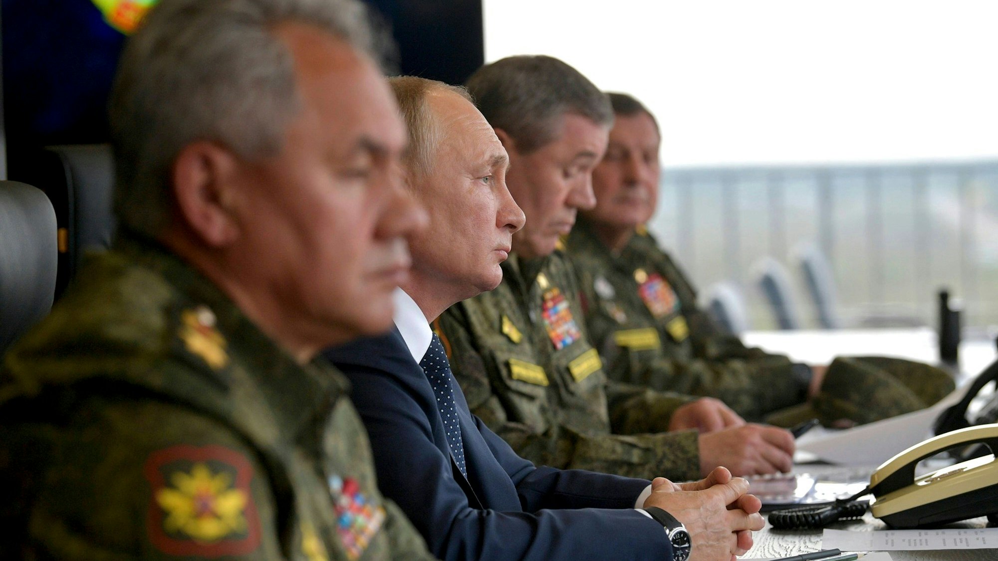 Putin sitzt neben mehreren Männern in Militäruniformen mit Abzeichen an einem Besprechungstisch.
