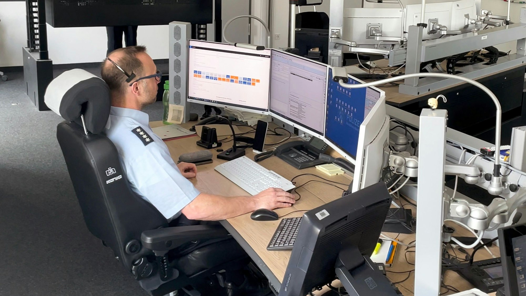 Ein Polizist in Uniform sitzt an einem Computerarbeitsplatz vor vier Bildschirmen.