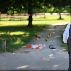 Ein Polizist steht vor einem Park, der mit Absperrband abgesichert wurde.