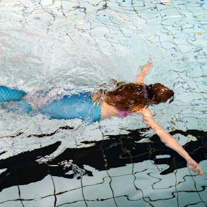 Ein Mädchen schwimmt als Meerjungfrau mit einer Flosse in einem Schwimmbecken eines Hallenbades.