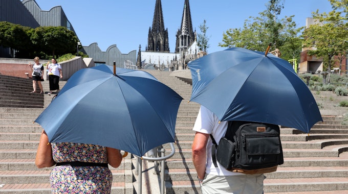 Zwei Touristen schützen sich mit Regenschirmen vor der Sonne.