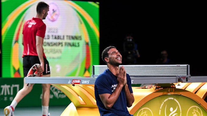 Ein Tischtennisspieler kniet mit betenden Händen auf dem Boden vor einer Tischtennisplatte und schaut lachend nach oben.&nbsp;