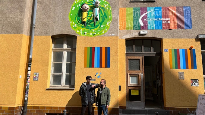 Yaşar Fidan (l.) und Lemi Karaca von Coach e.V. stehen vor ihrem Kunstwerk am Allerweltshaus in Ehrenfeld. Die 3D-Installation zeigt Rick und Morty aus der gleichnamigen Serie, wie sie aus einem Portal kommen.