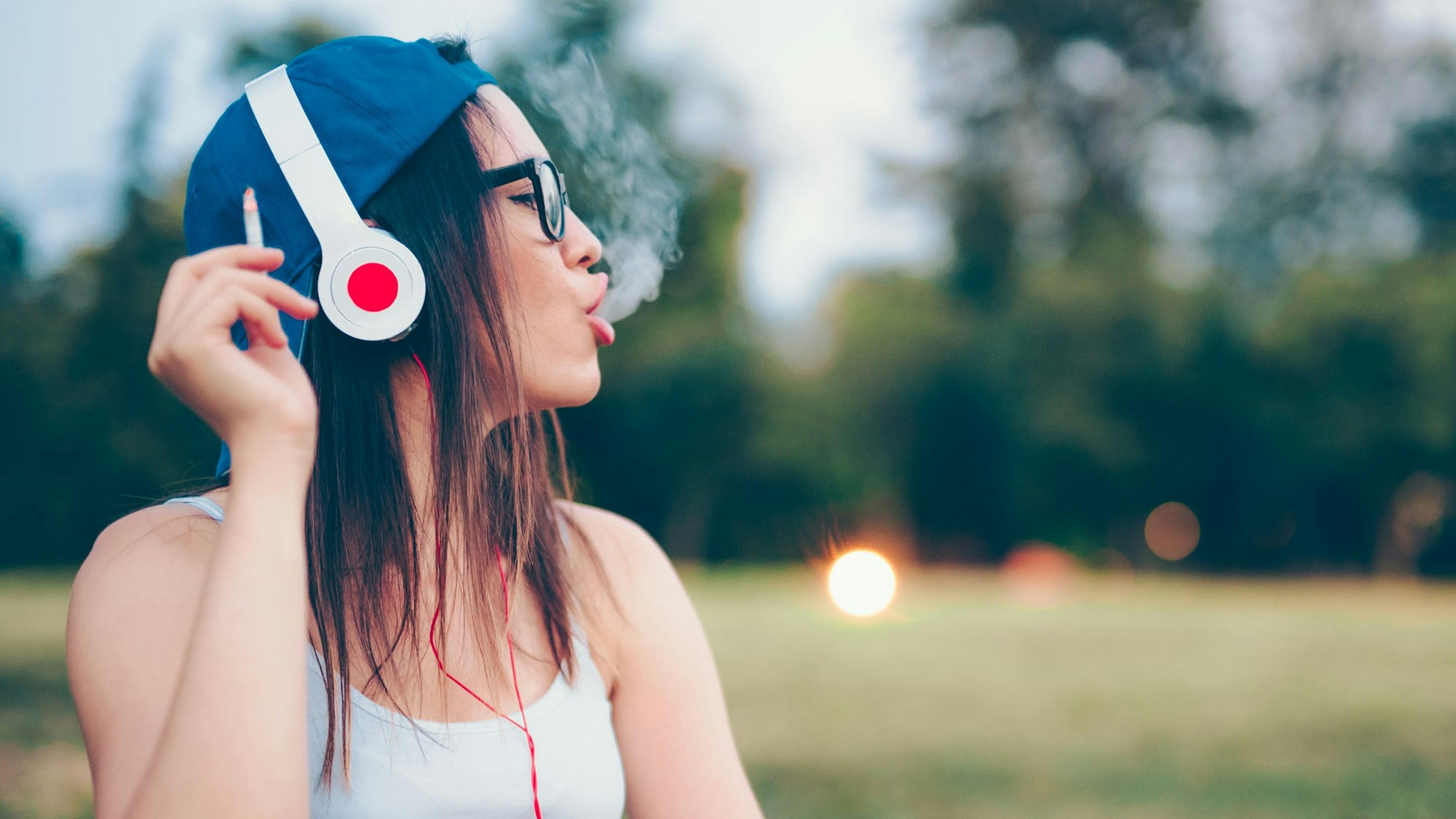 junge Frau mit Kopfhörern und Zigarette im Park