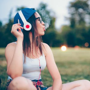 junge Frau mit Kopfhörern und Zigarette im Park