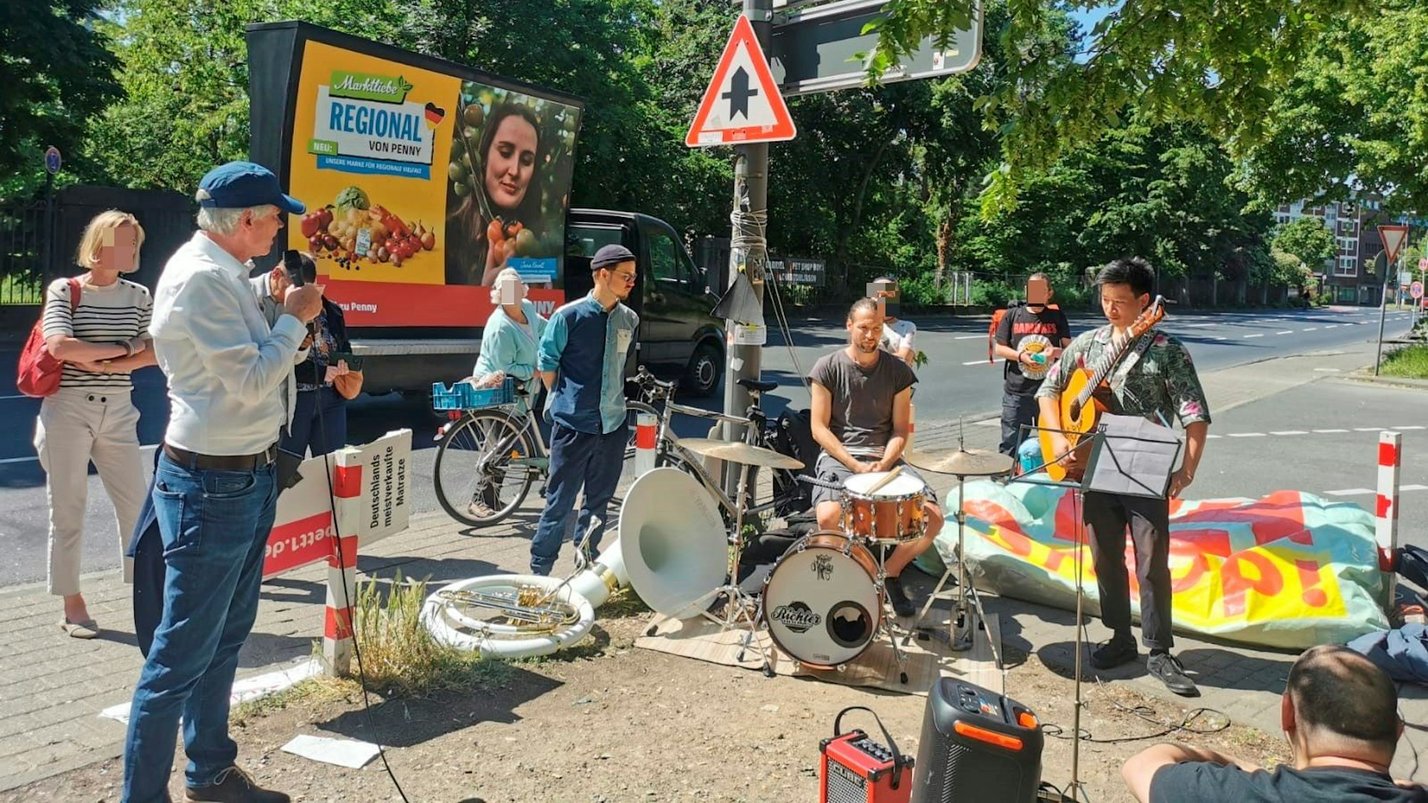 Eine Band spielt am Gehweg vor dem OMZ-Haus, dabei steht ein Mann mit Mikrofon. Eine handvoll Passantinnen und Passanten sind stehen geblieben.