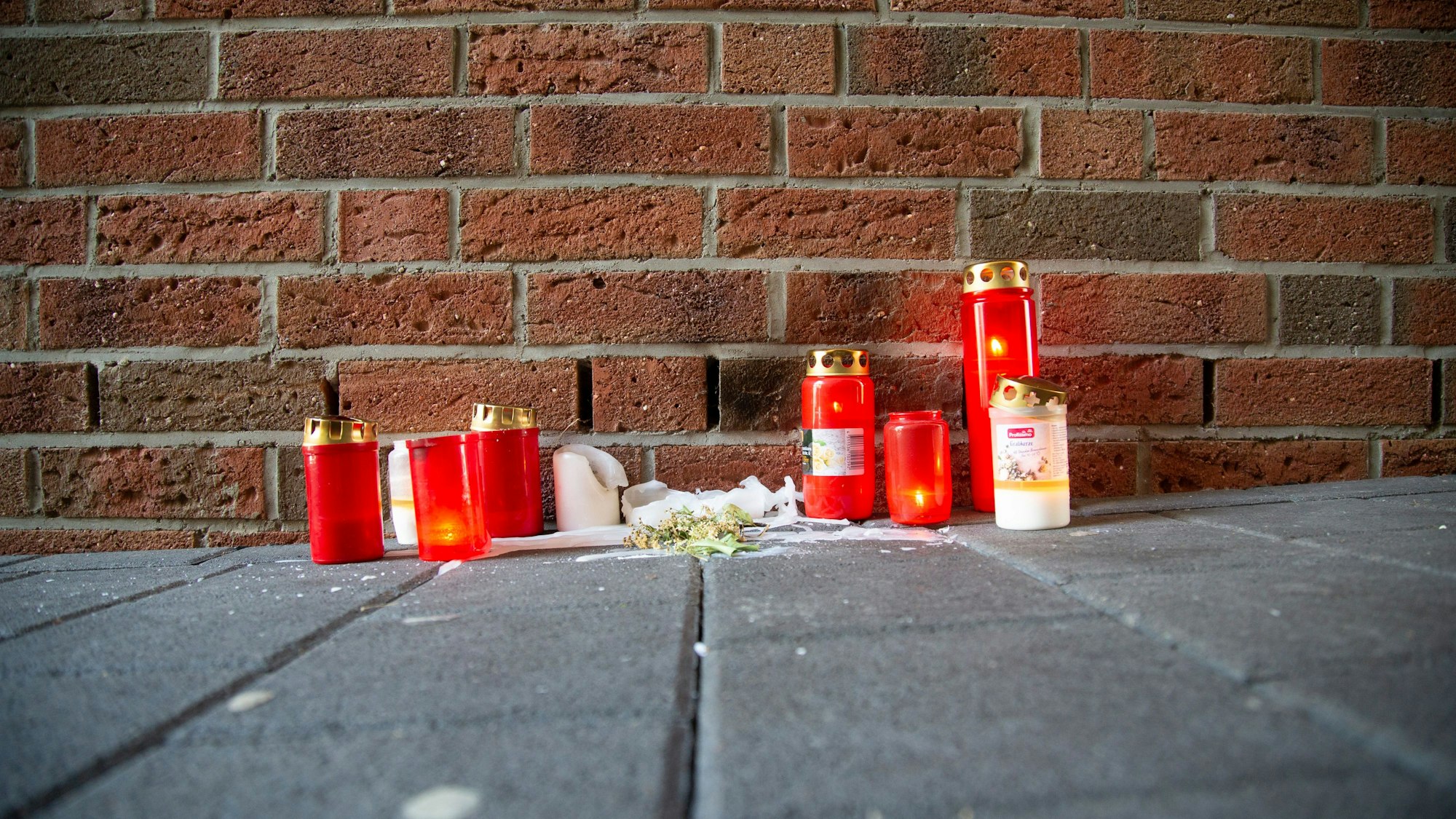 Kerzen stehen am Tatort in Köln-Mülheim vor einer Backsteinwand.