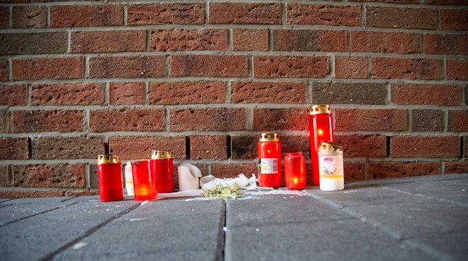 Kerzen stehen am Tatort in Köln-Mülheim vor einer Backsteinwand.