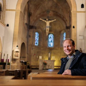 Der Priesteramtsanwärter Sebastian Appolt sitzt auf einer Bank in der Kirche St. Gertrudis und lächelt in die Kamera.