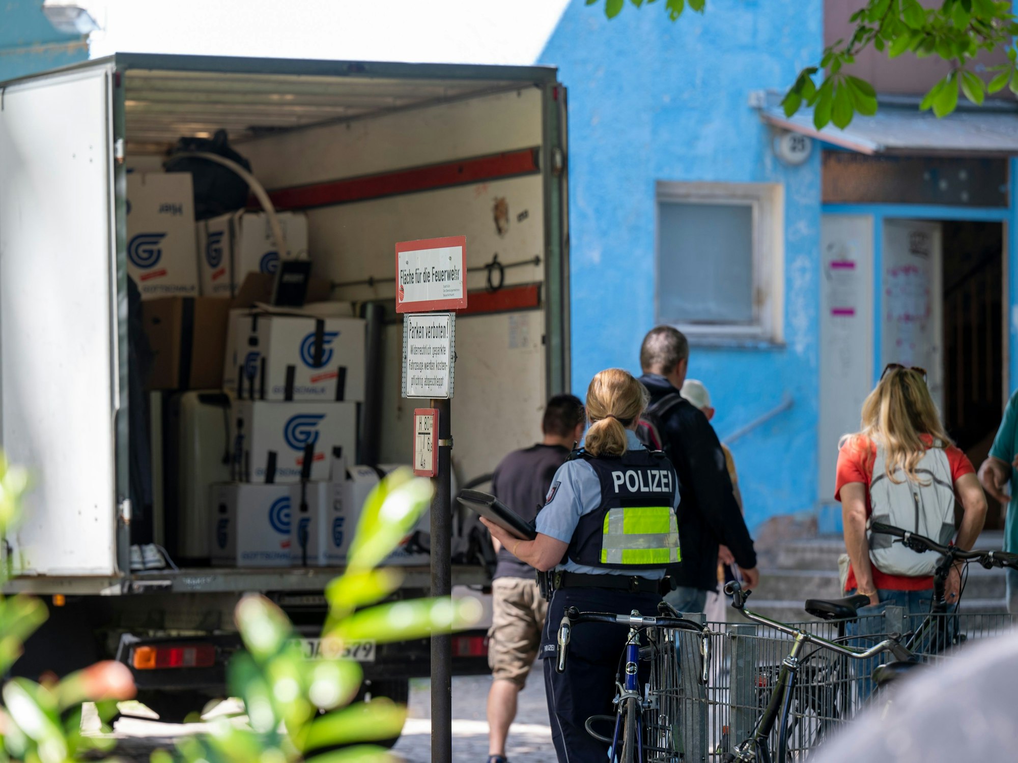 Ein Umzugswagen steht vor dem Haus, mehrere Personen, darunter eine Polizistin stehen davor.
