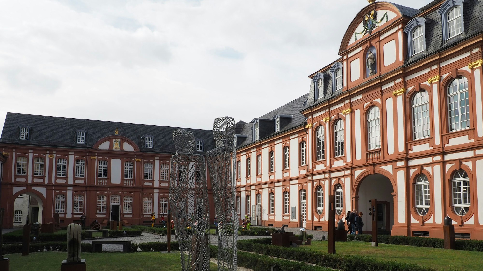 Zu sehen ist die Abtei Brauweiler mit ihrer weißen und terracotta-farbenen Fassade und einem Teil des Innenhofs.