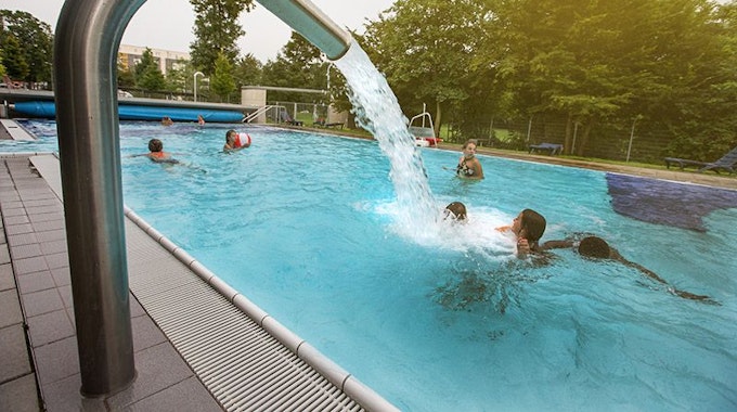 Bei der Aufnahme des Vierjahreszeitenbeckens des Ossendorfbads schießt Wasser aus einem Rohr am Seitenrand und begießt Badegäste im Becken.