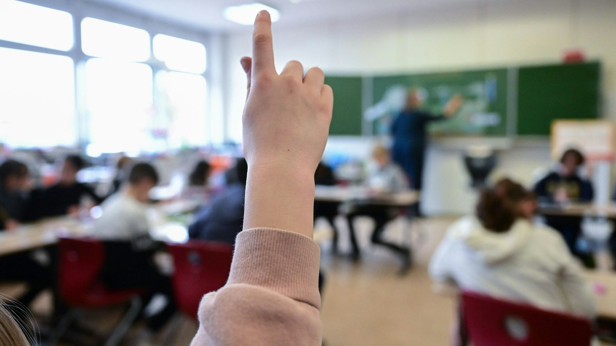 Ein Kind hebt in einem Klassenzimmer die Hand, um sich zu melden.