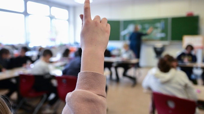 Ein Kind hebt in einer vollbesetzten Klasse den Finger.