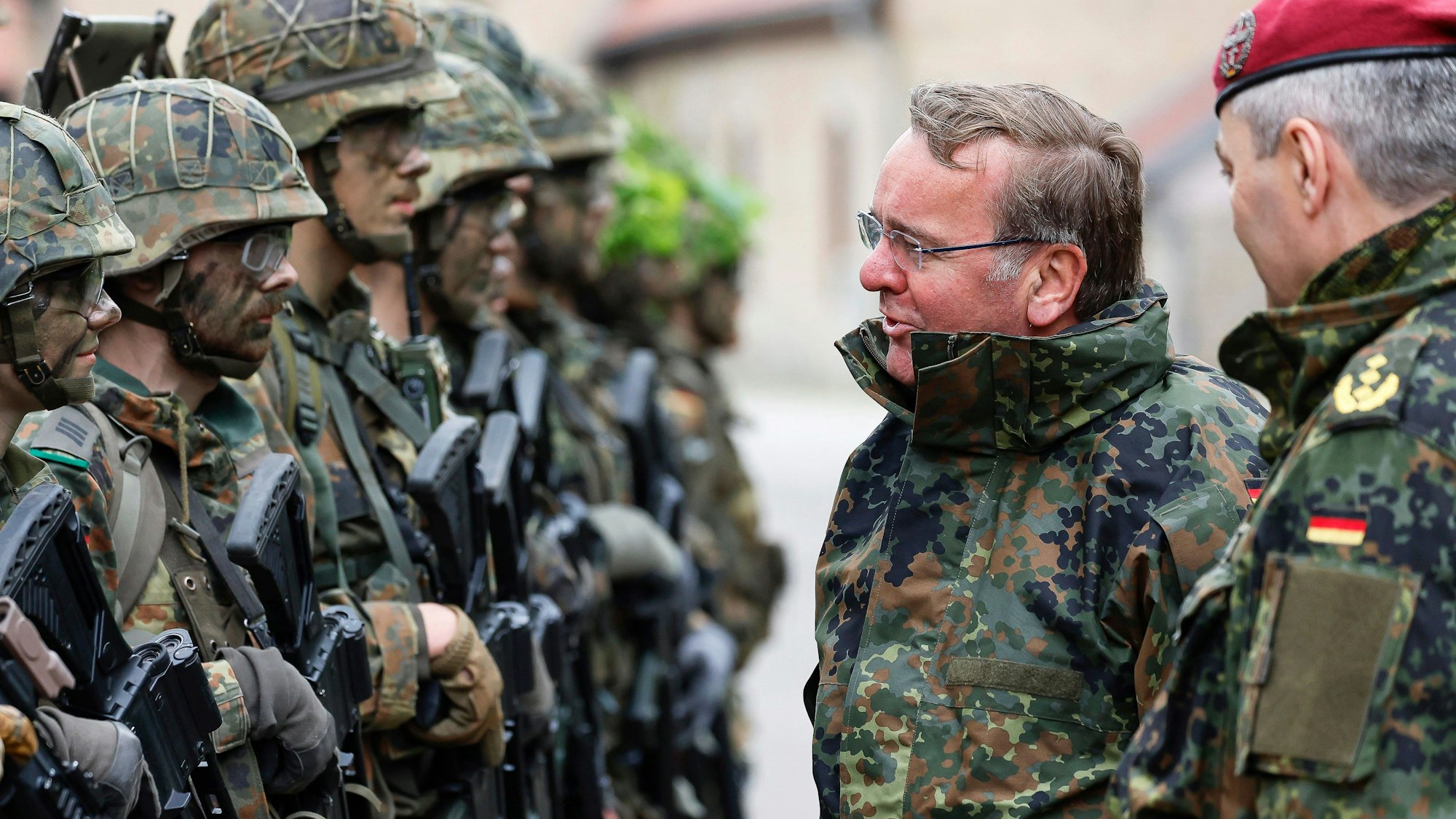 Es ist Boris Pistorius in Kleidung der Bundeswehr zu sehen. Er ist umgeben von mehreren Soldaten.
