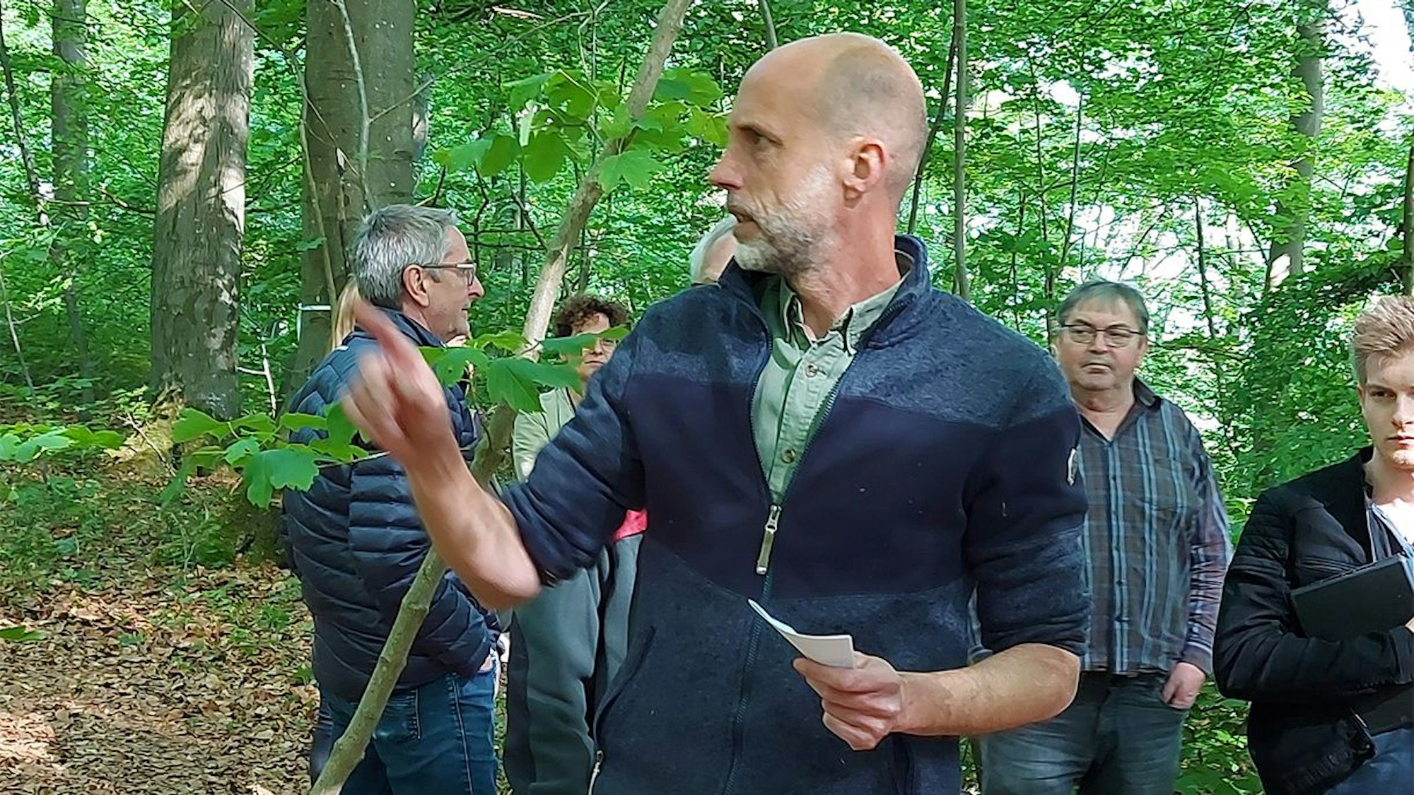 Das Bild zeigt den Förster Tobias Peulen, der einer Gruppe Menschen im Wald etwas erklärt.