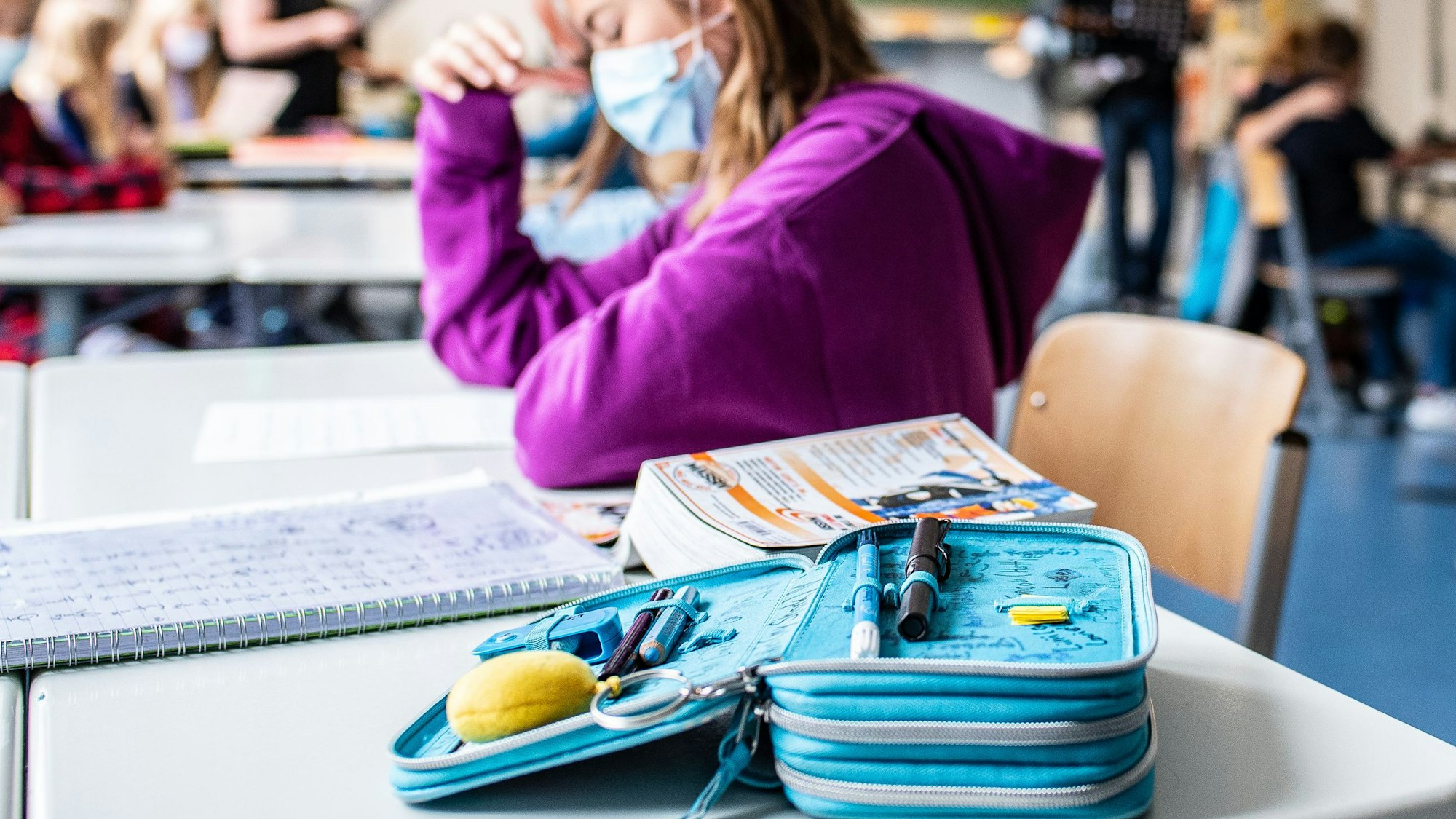 Eine Schülerin sitzt mit ihrer Maske neben ihrem Etui, das auf ihrem Tisch liegt.