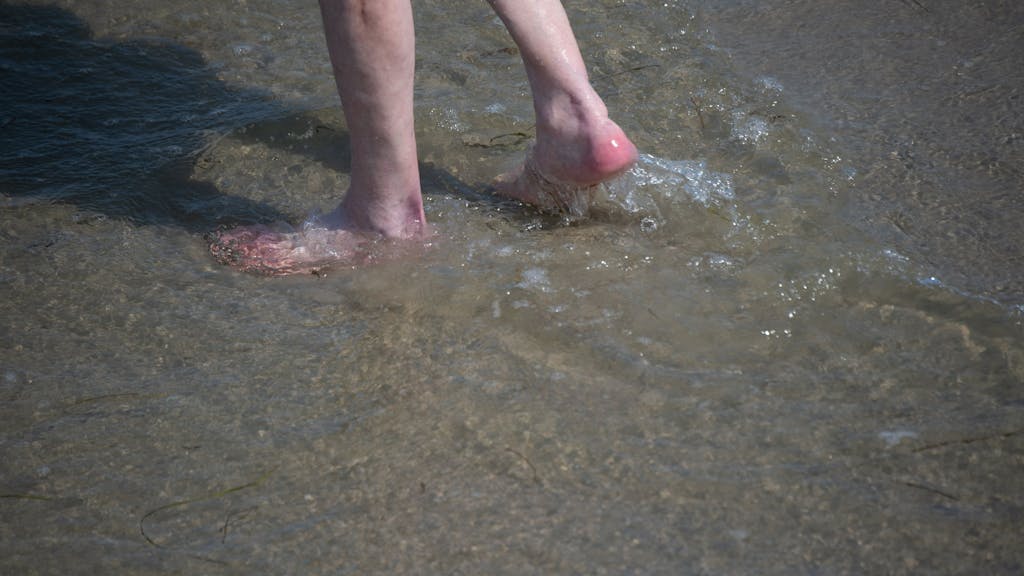 Ein Mann watet im Sommer 2021 durch das flache Wasser am Strand des Seebads. Viele Ostseebäder machten damals mit Aushängen auf die Gefahr durch Vibrionen aufmerksam. Diese Gefahr könnte laut RKI zunehmen.