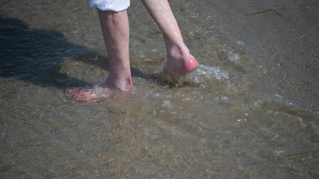 Ein Mann watet im Sommer 2021 durch das flache Wasser am Strand des Seebads. Viele Ostseebäder machten damals mit Aushängen auf die Gefahr durch Vibrionen aufmerksam. Diese Gefahr könnte laut RKI zunehmen.