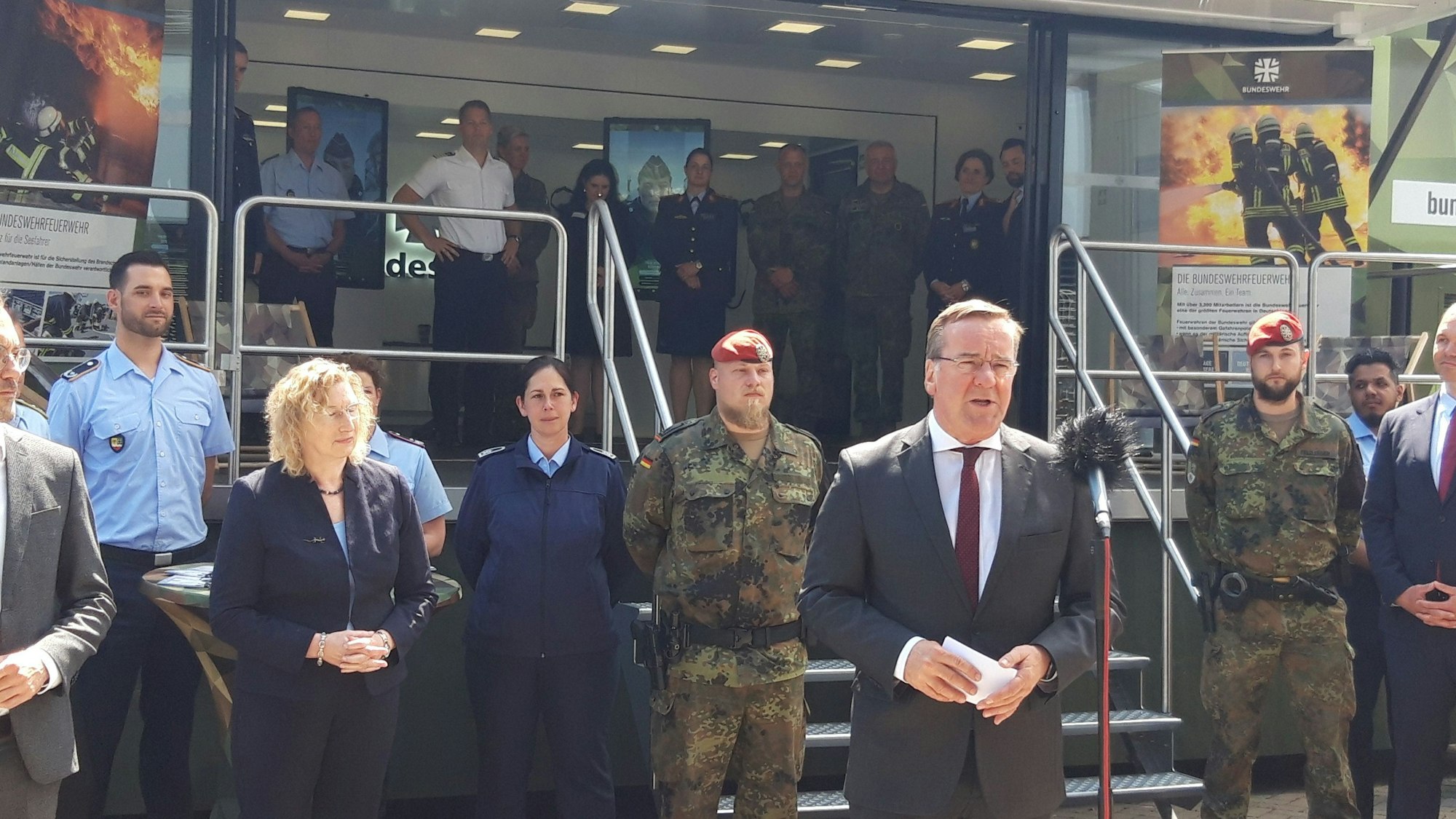 Bundesverteidigungsminister Boris Pistorius spricht in ein Mikrofon, im Hintergrund Angehörige der Kölner Lüttich-Kaserne und ein Karrieretruck der Bundeswehr.
