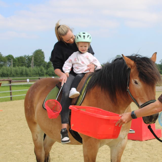 Auf dem Pferd ist zu sehen, wie Sarah Strupp und ihre Tochter Lena auf dem Rücken von „Moritz “den Parcours meistern. Thomas Görs hilft ihnen dabei.