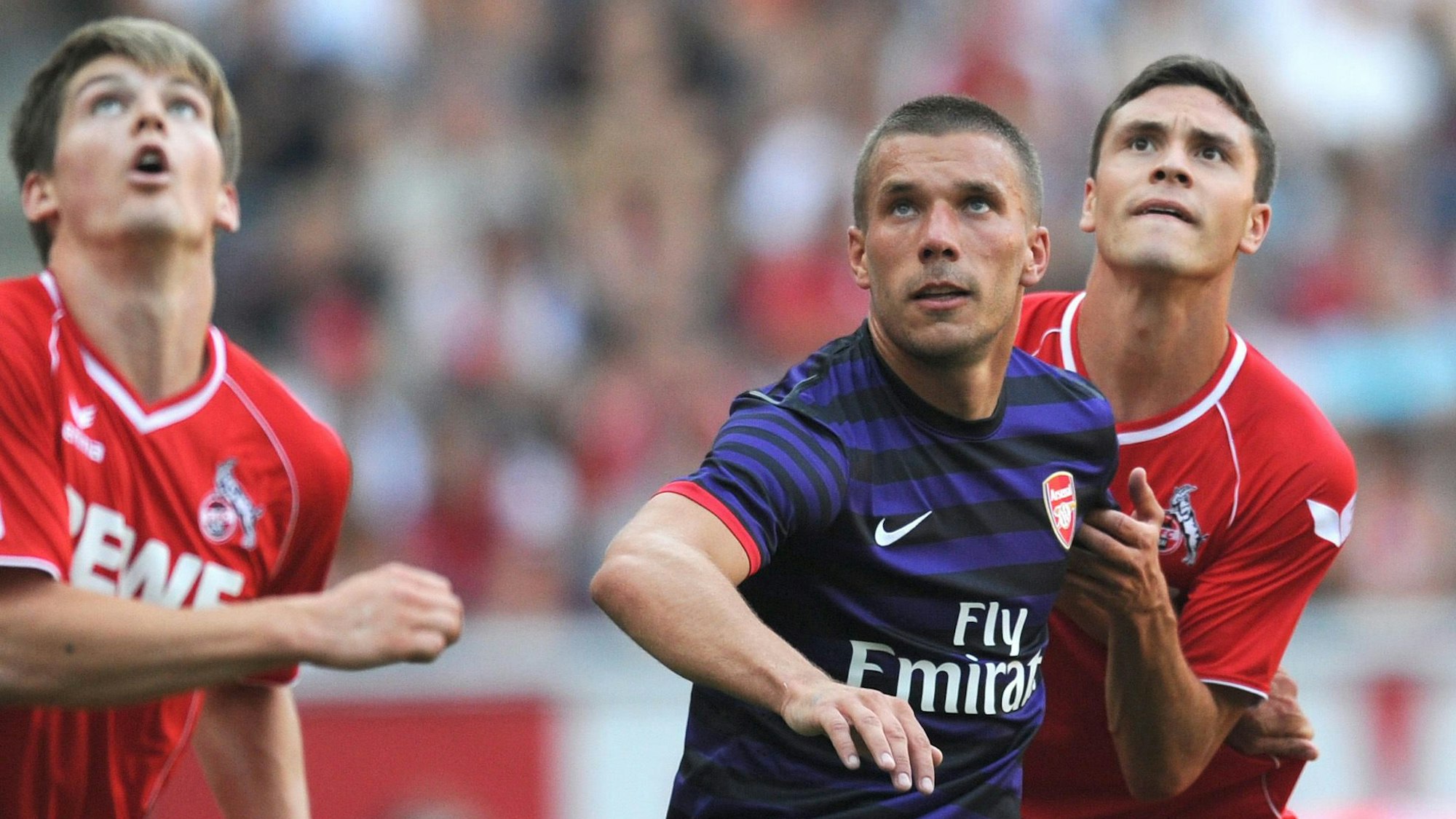Lukas Podolski (M.) vom FC Arsenal wehrt sich im August 2012 im Testspiel gegen Jonas Hector (r.) vom 1. FC Köln, Lukas Kübler (l.) schaut zu.