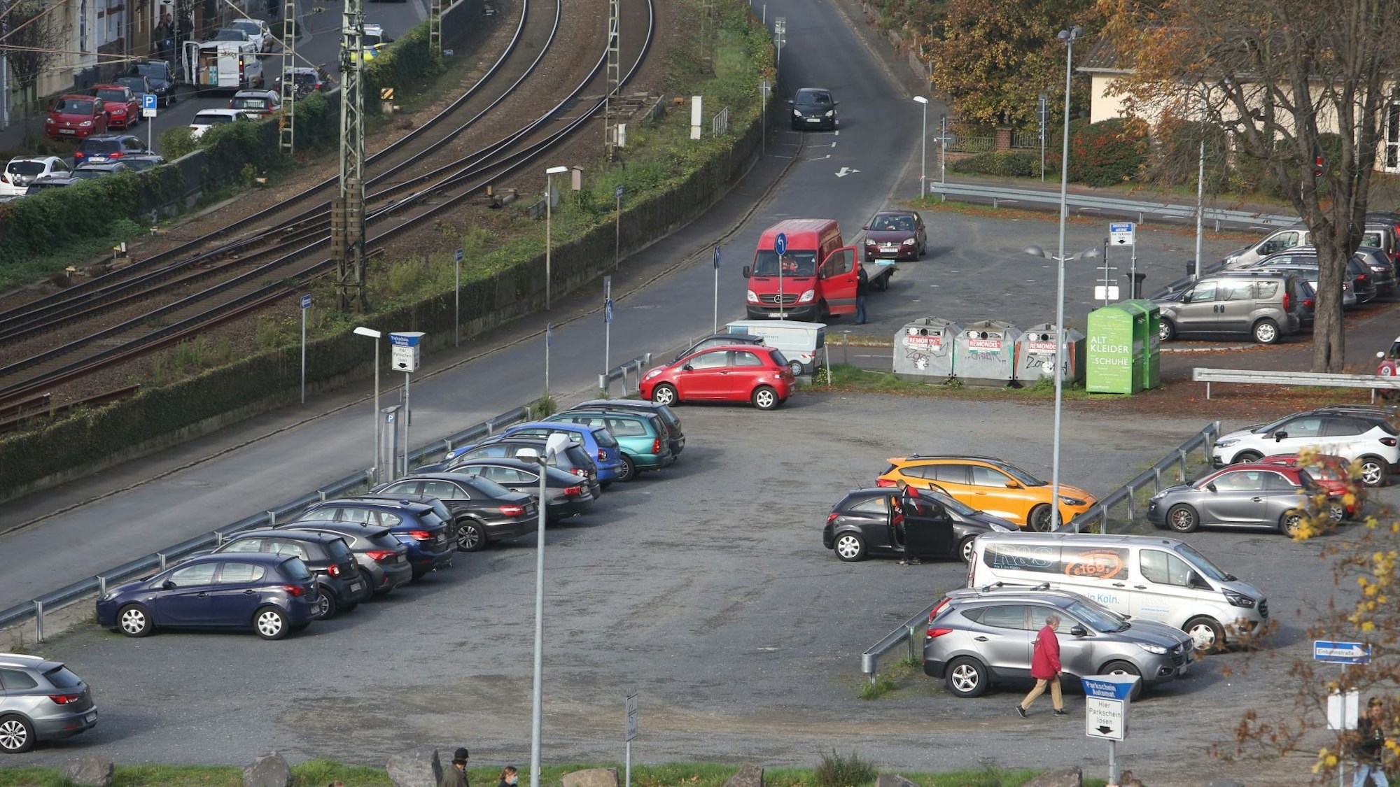 Parkende Autos stehen auf einer Schotterfläche. Links am Bildrand verläuft die rechtsrheinische Bahntrasse.