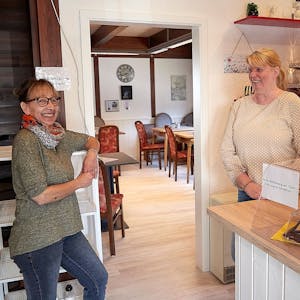 Das Bild zeigt zwei Frauen, die in einem Café an einem Regal und einer Theke stehen.