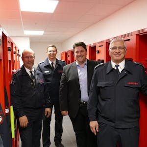 Zu sehen sind Löschgruppenführer Ralf Eich, Leiter der Troisdorfer Feuerwehr, Lars Gödel, Bürgermeister Alexander Biber und Löschgruppenführer Salvatore Rizzello zwischen roten Schränken.