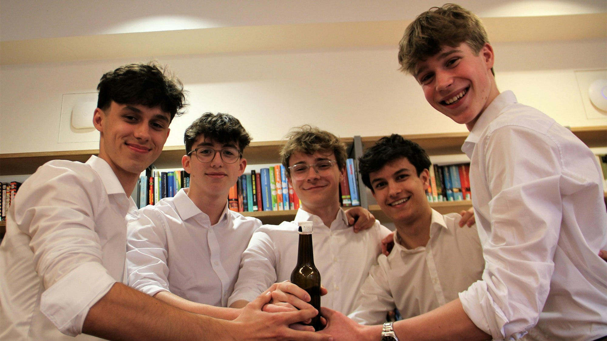 Fünf junge Männer halten gemeinsam eine Bierflasche.