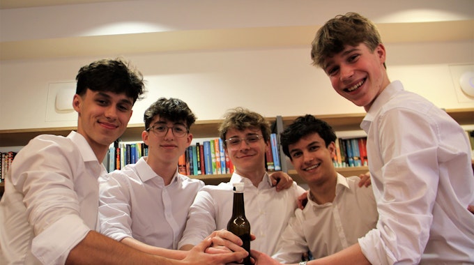 Fünf junge Männer halten gemeinsam eine Bierflasche.&nbsp;