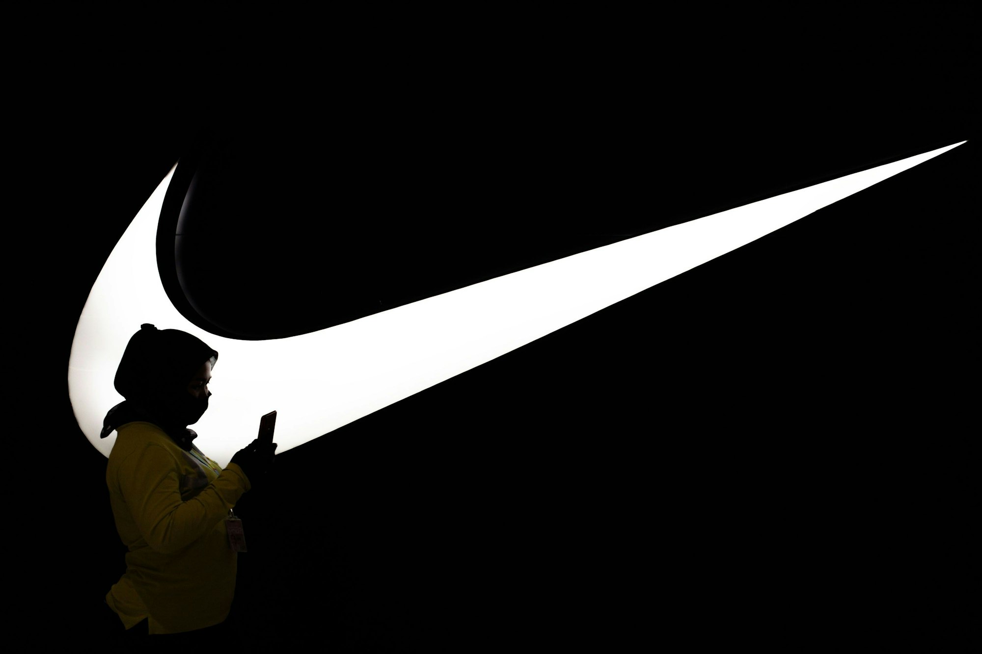 Frau steht vor einem großen, beleuchteten Nike Logo. Bild zum Nike Sale Artikel.